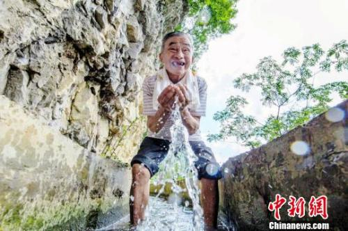 资料图：黄大发十分开心地捧起水渠里流淌的泉水。　田维野 摄