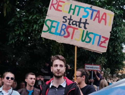 　　反纳粹抗议者举的牌子上写着“法治而非维吉兰特正义（vigilante justice，非执法人员私自执法）”。 图自外媒