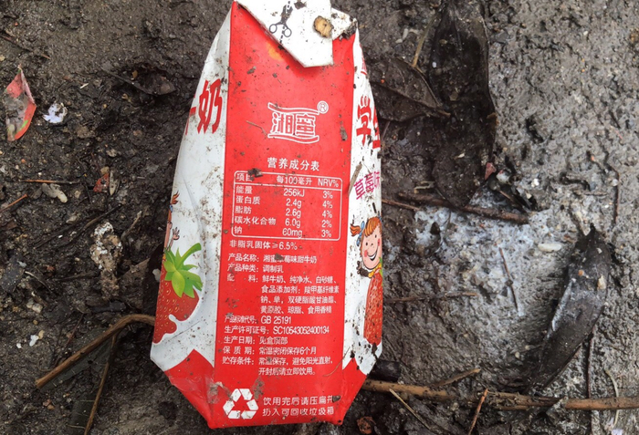 在校外的垃圾箱旁边可看到许多“湘蜜”牌牛奶盒，地面有牛奶溢出痕迹。&nbsp;受访者供图