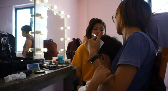 化妆师一边给俊昊化妆，俊昊一边看小猪佩奇。