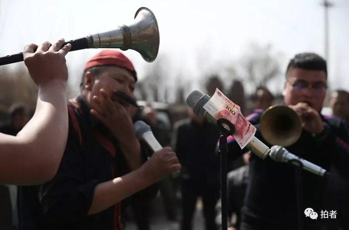  △&nbsp;三平（红帽子）正在表演口技，麦克风上夹着主家给的赏钱。