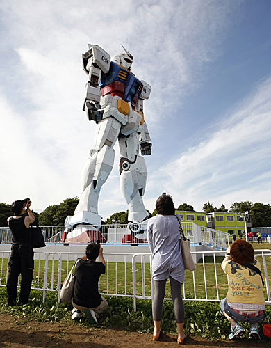 在日本首都东京的一座公园内，游客给高达18米的“高达”模型拍照。（新华社）