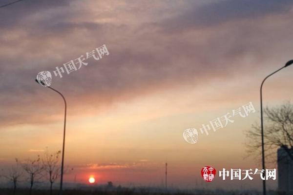 昨晨，北京能见度好转，初升的太阳将云彩映成粉色。