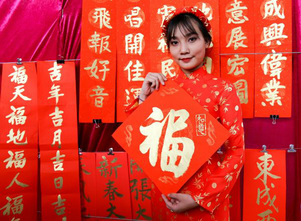 　　2017年春节前夕，在越南胡志明市举办的“慈善挥春”活动上，市民手持福字在春联前留影。（新华社）