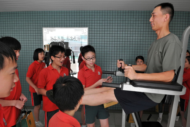 一名驻澳门部队士兵在给小学生示范使用健身器材